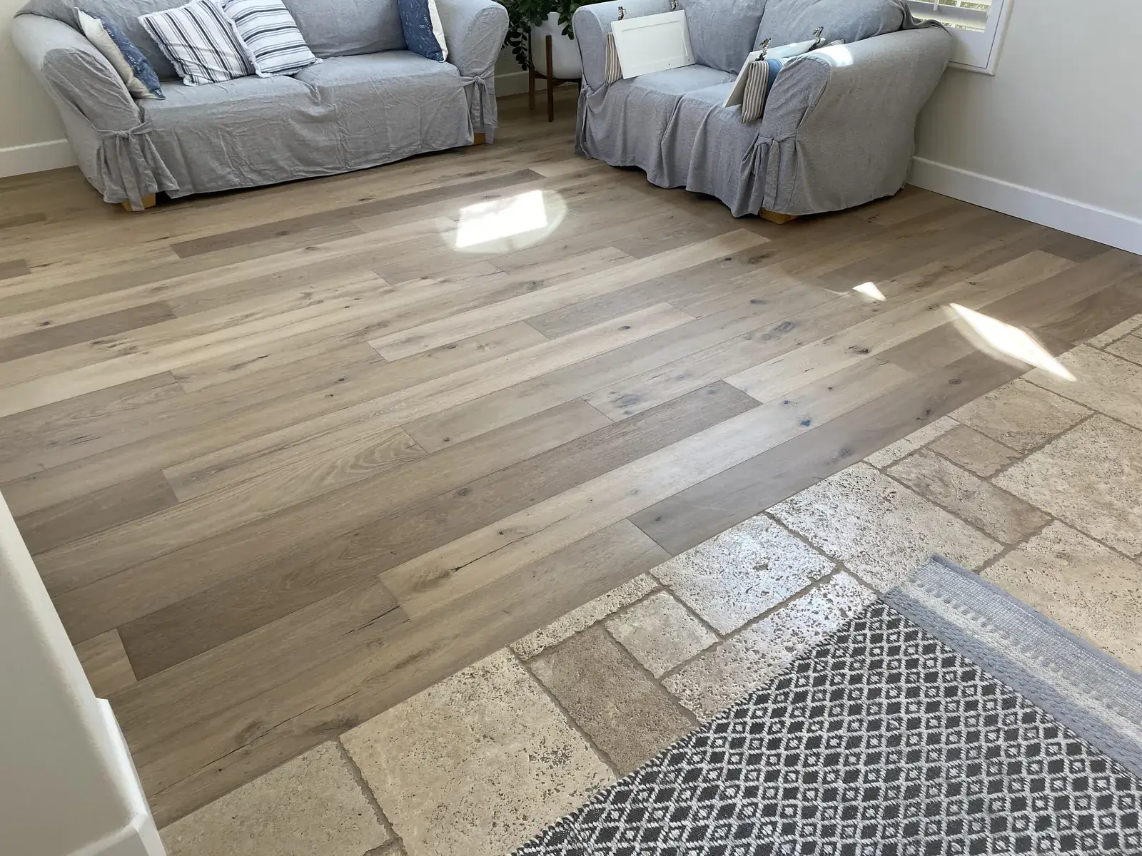 Wide-plank hardwood meeting a travertine tile border, flush transition.